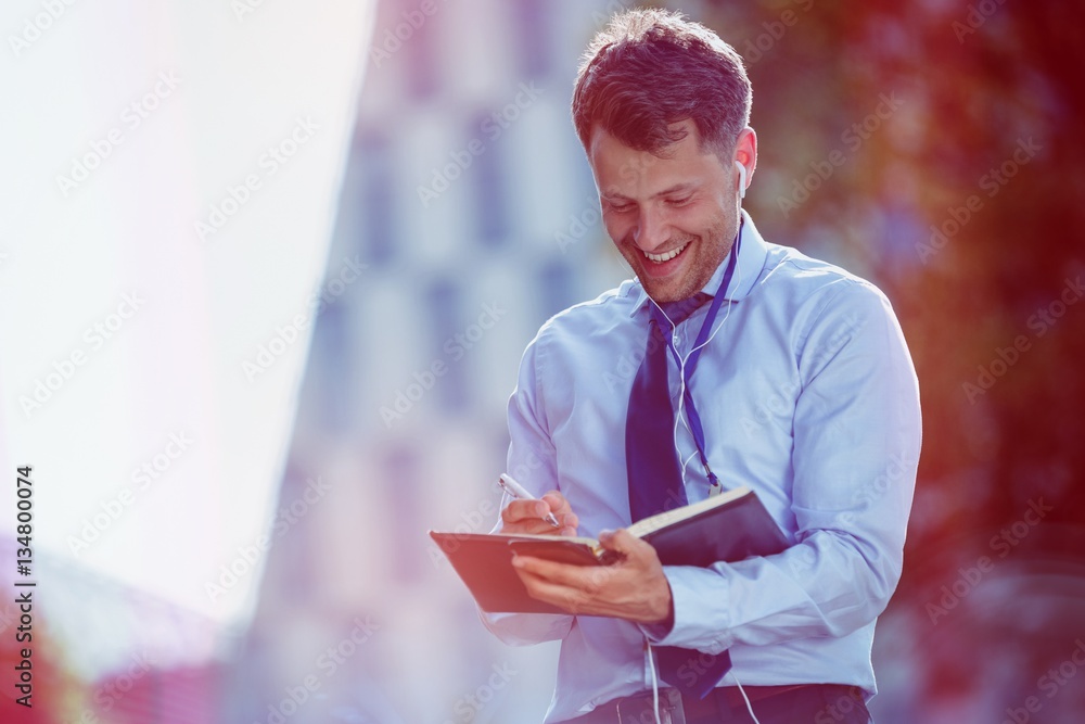 Cheerful businessman writing in dairy 