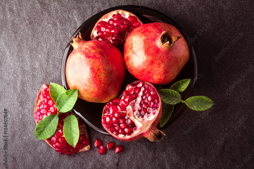 Fresh red pomegranate and seed  with leaves over black stone 