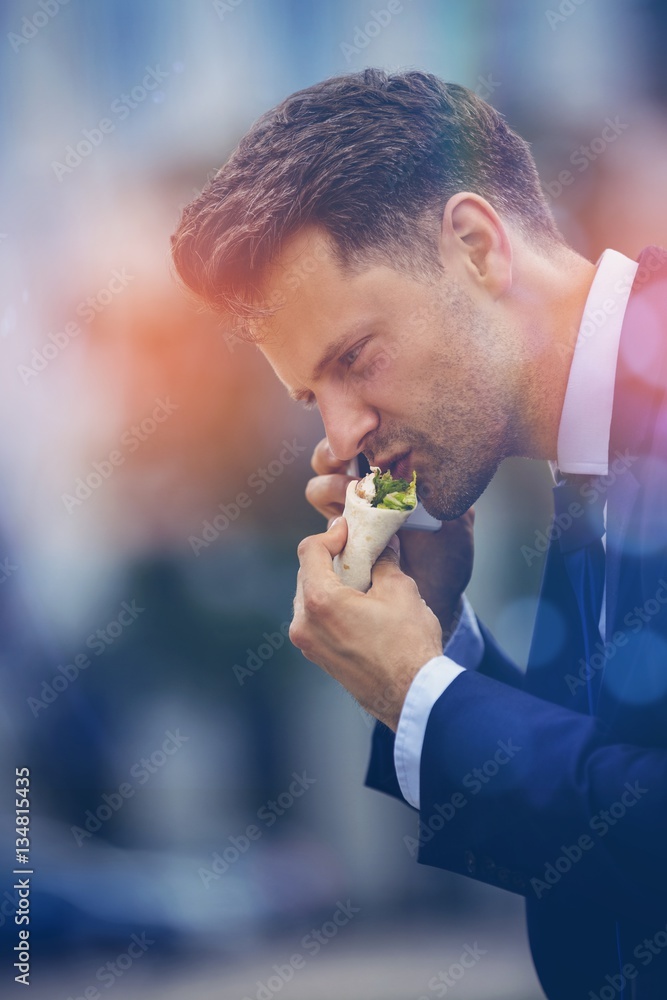 Handsome businessman eating snacks and talking on phone