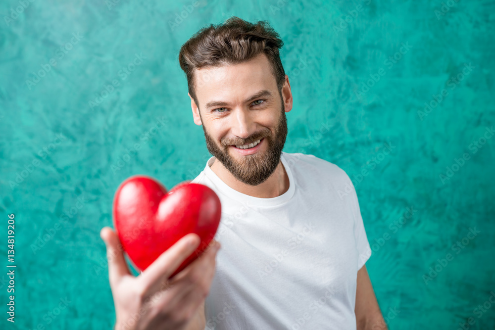 Handsome man in the white t-shirt giving red heart standing on the painted green wall background. Va