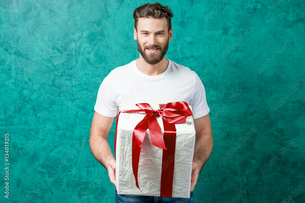 Handsome man in the white t-shirt holding gift box on the painted green wall background. Valentines