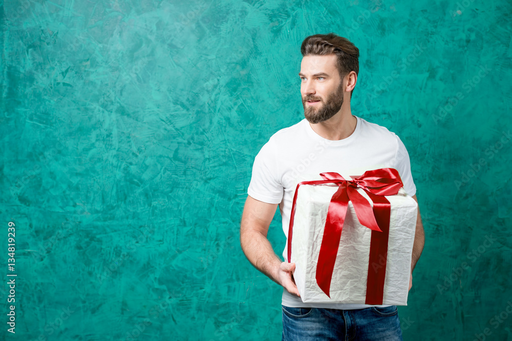 Handsome man in the white t-shirt holding gift box on the painted green wall background. Valentines