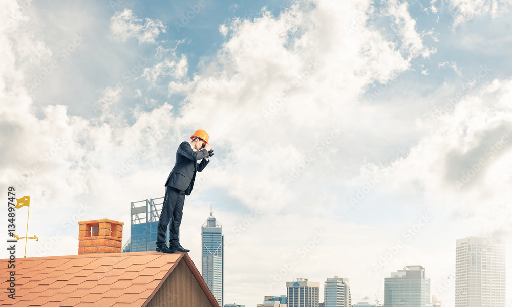 Engineer man standing on roof and looking in binoculars. Mixed m