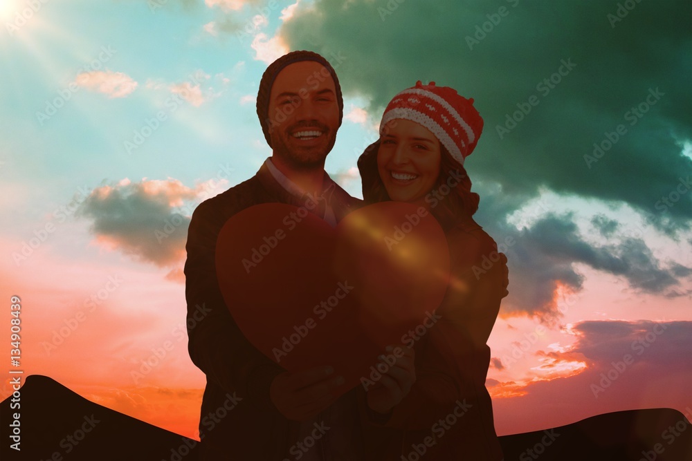 Composite image of happy young couple holding heart shape paper