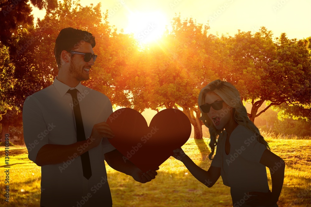 Composite image of cool young couple holding red heart