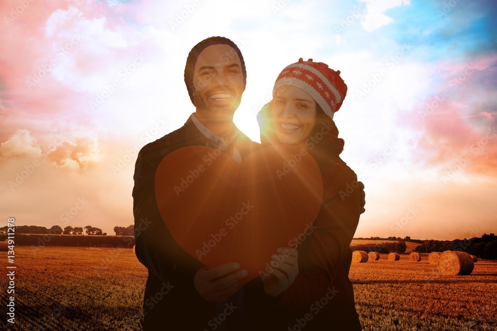 Composite image of happy young couple holding heart shape paper