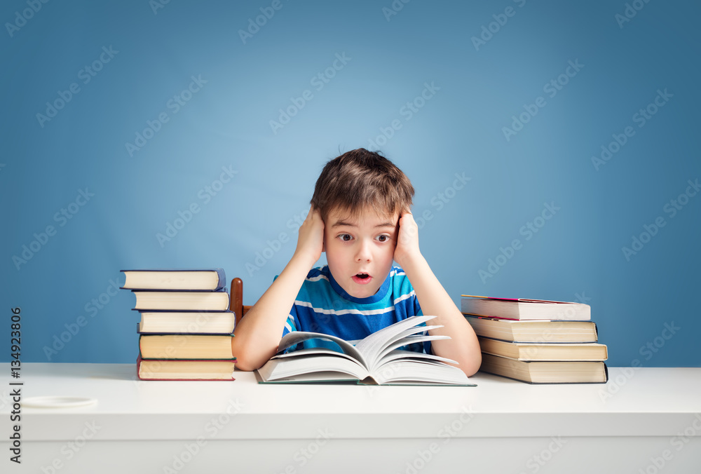 seven years old child reading a book at home. Boy studing at table on blue background