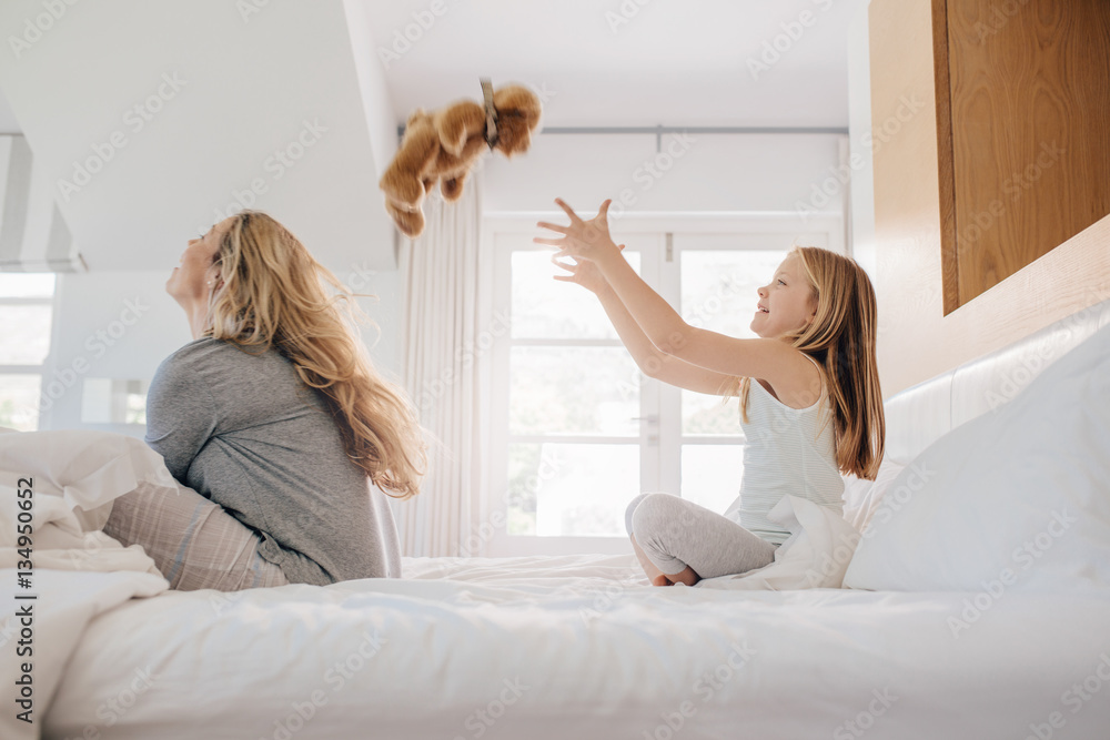 Mother and daughter playing with teddy bear on bed