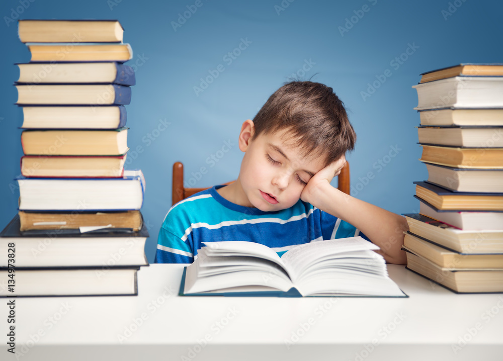 seven years old child reading a book at home. Boy studing at table on blue background