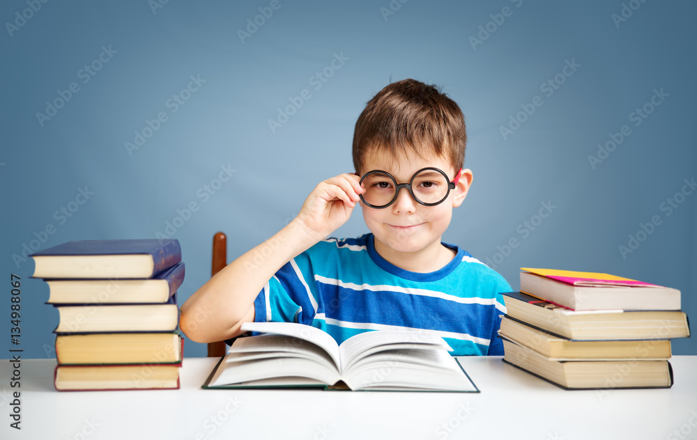 seven years old child reading a book at home. Boy studing at table on blue background