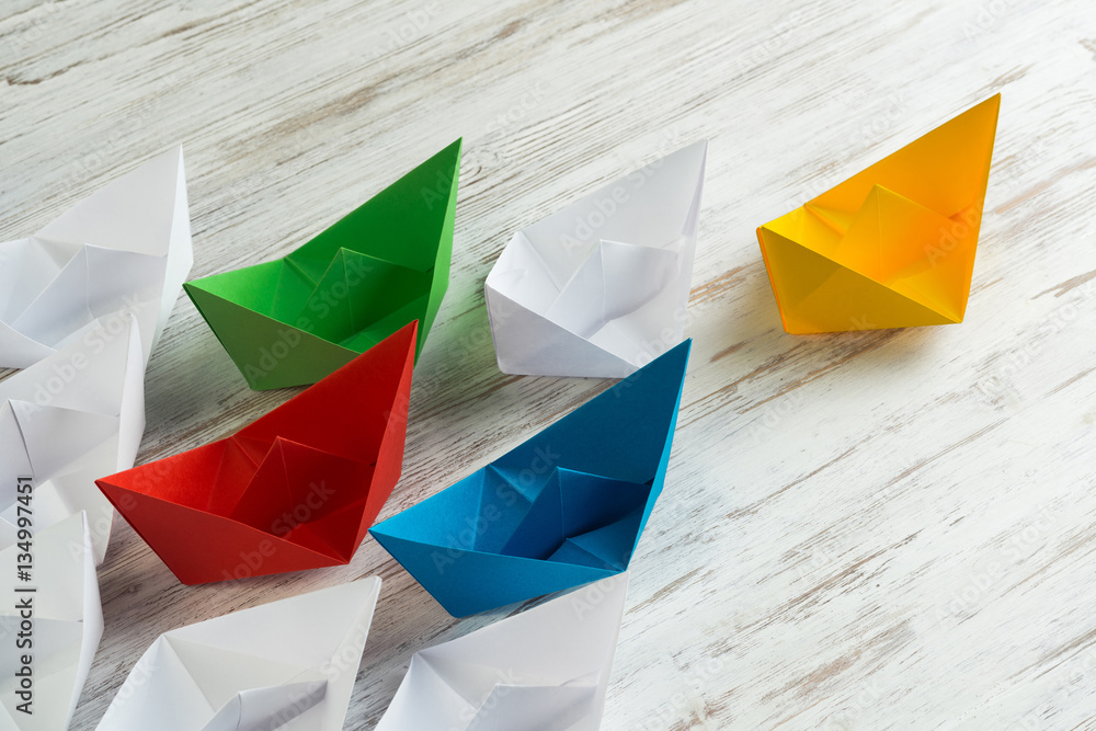 Business leadership concept with white and color paper boats on wooden table