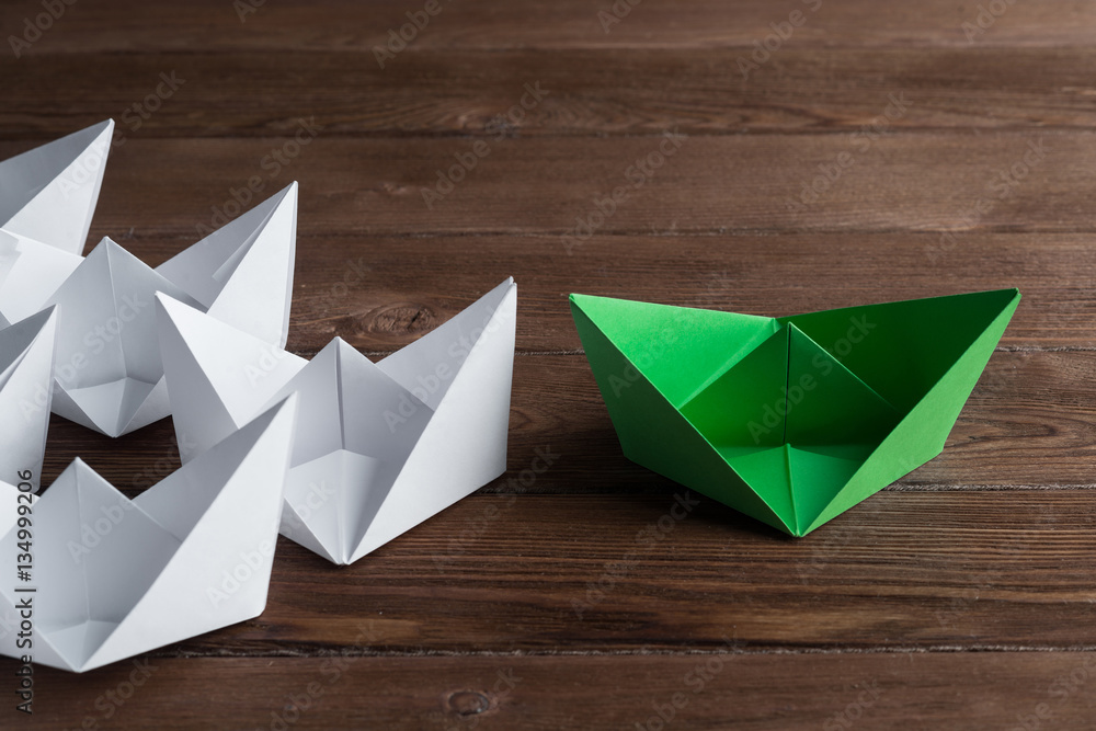 Business leadership concept with white and color paper boats on wooden table