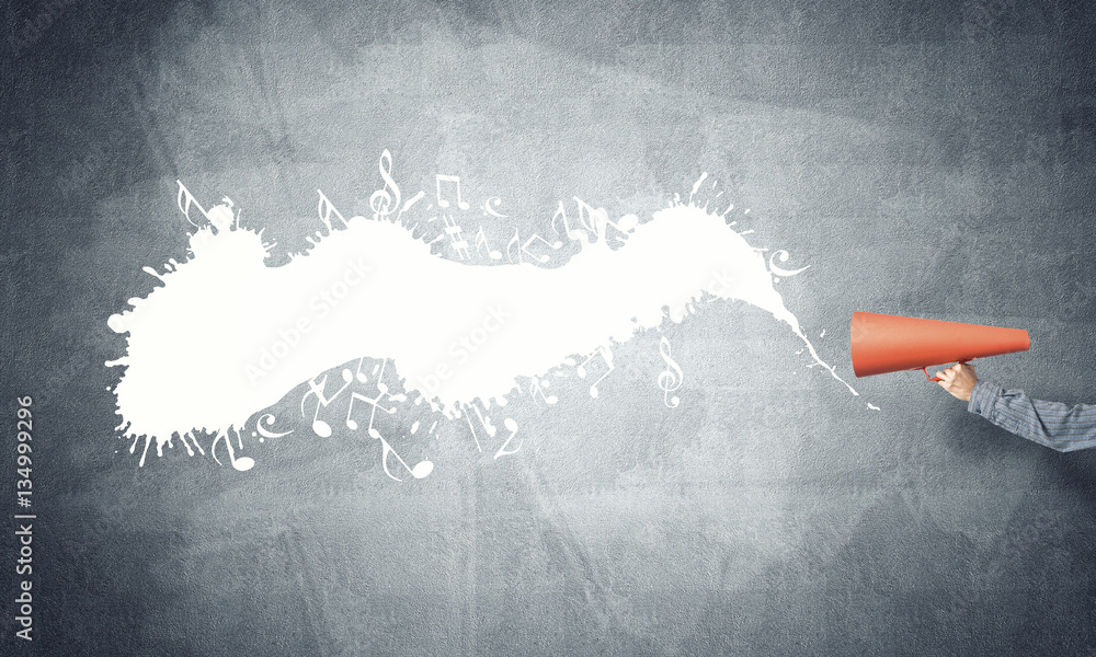 Hand of man holding orange paper trumpet against concrete background