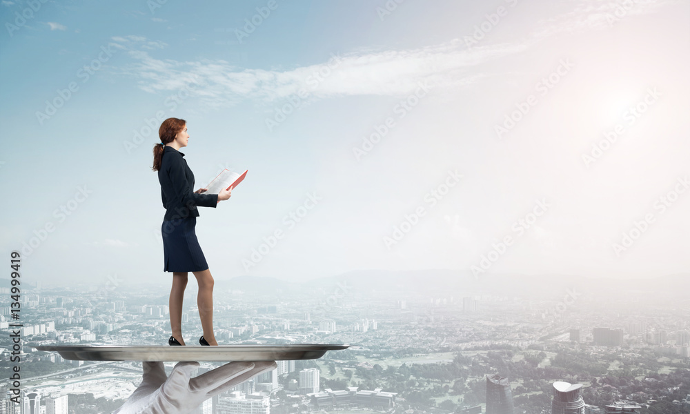 Attractive businesswoman on metal tray with red book in hands against cityscape background