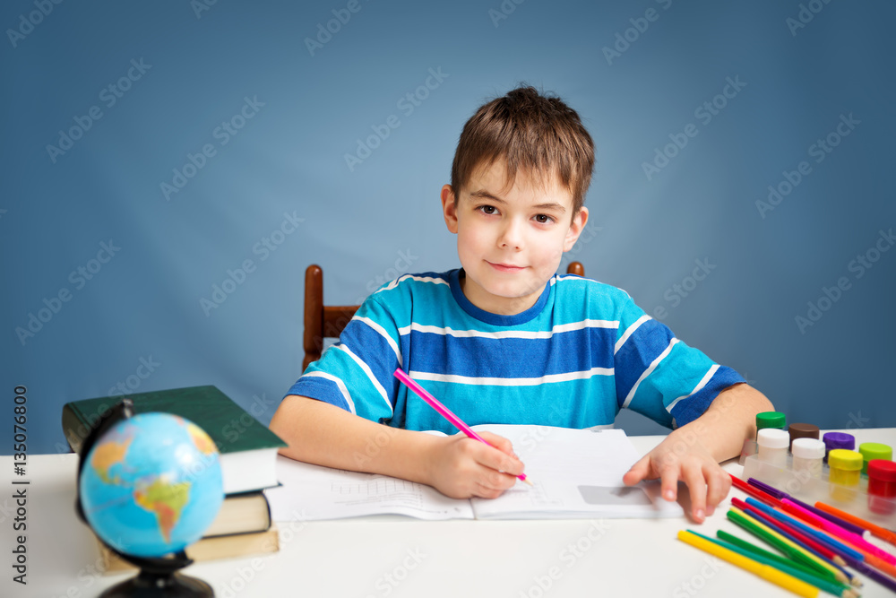 seven years old child writing at home. Boy studying at table on blue background. Kid drawing with a 