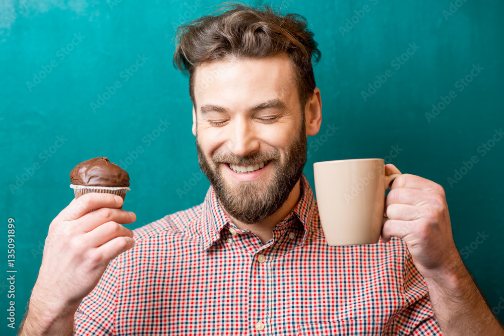 Close-up portrait of a man with chocolate muffin and coffee cup on the green background