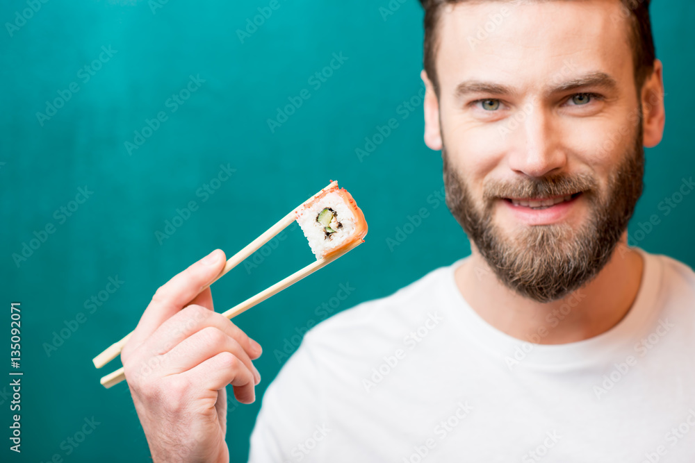 Close-up portrait of a man holding sushi with chopsticks on the green background. Image focused on t