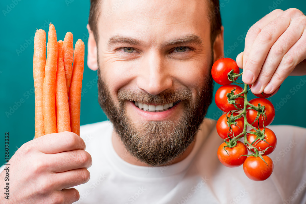 Close-up portrait of a handsome bearded man with vegetables on the green background