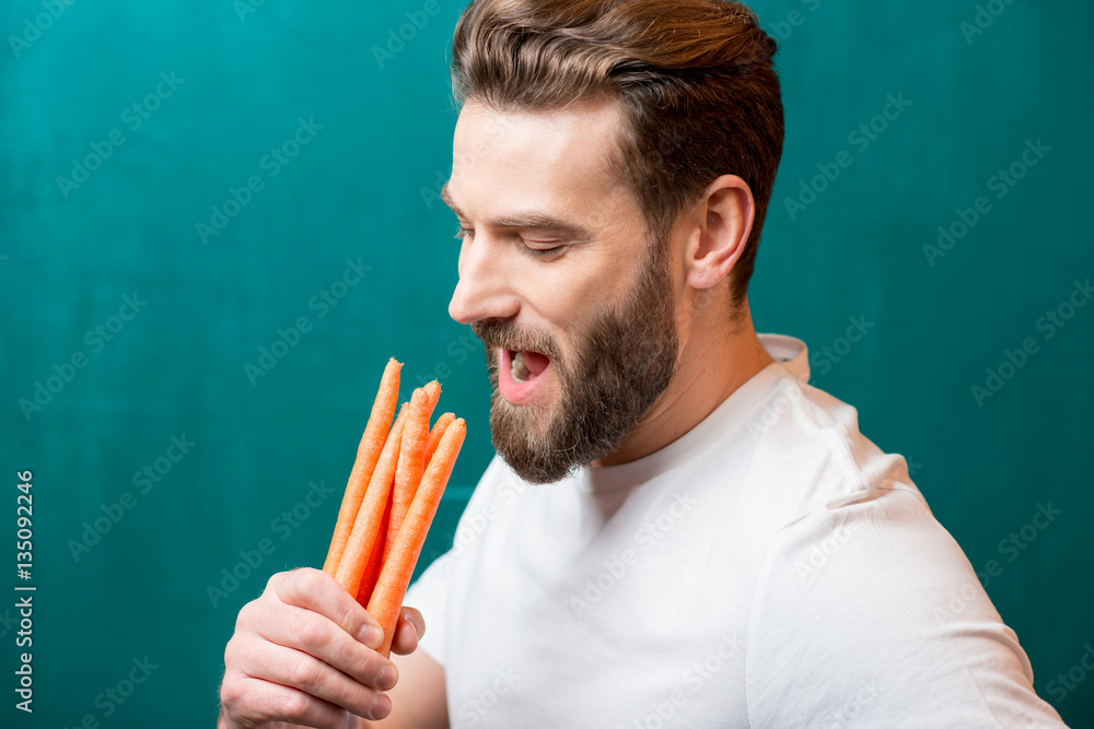 Close-up portrait of a handsome bearded man with mini carrots on the green background