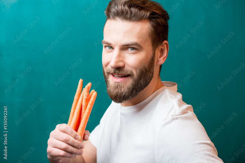 Close-up portrait of a handsome bearded man with mini carrots on the green background