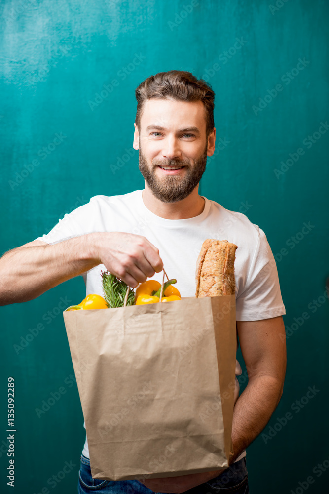 Handsome man holding a paper bag full of healthy food on the green background