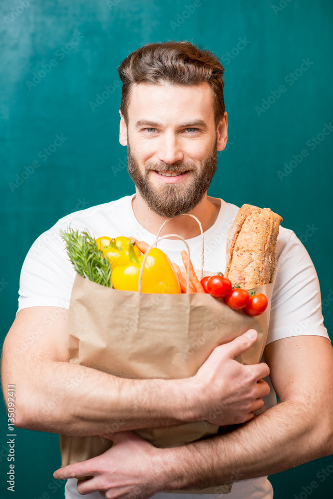 Handsome man holding a paper bag full of healthy food on the green background