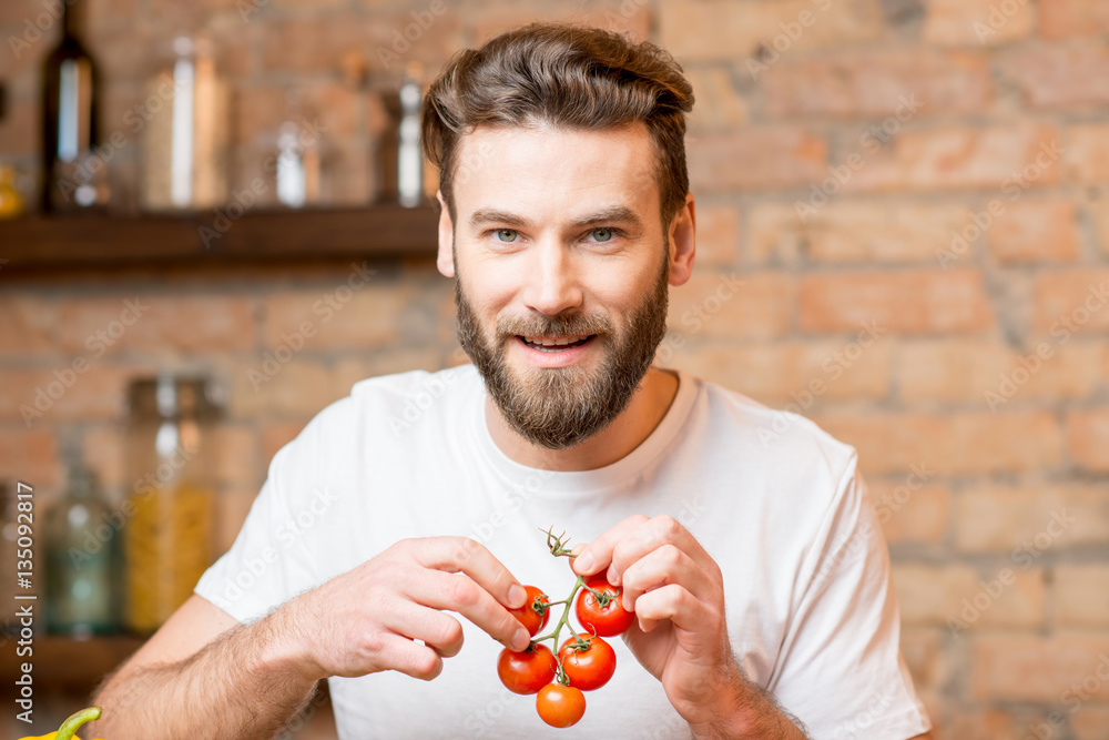 Handsome bearded man in white t-shirt making salad with tomatoes in the kitchen. Healthy and vegan f