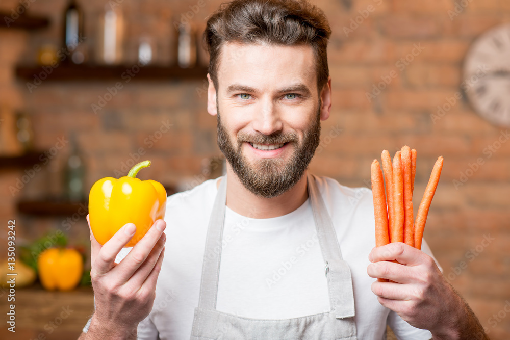 Portrait of a healthy man holding yellow pepper and carrot on the kitchen