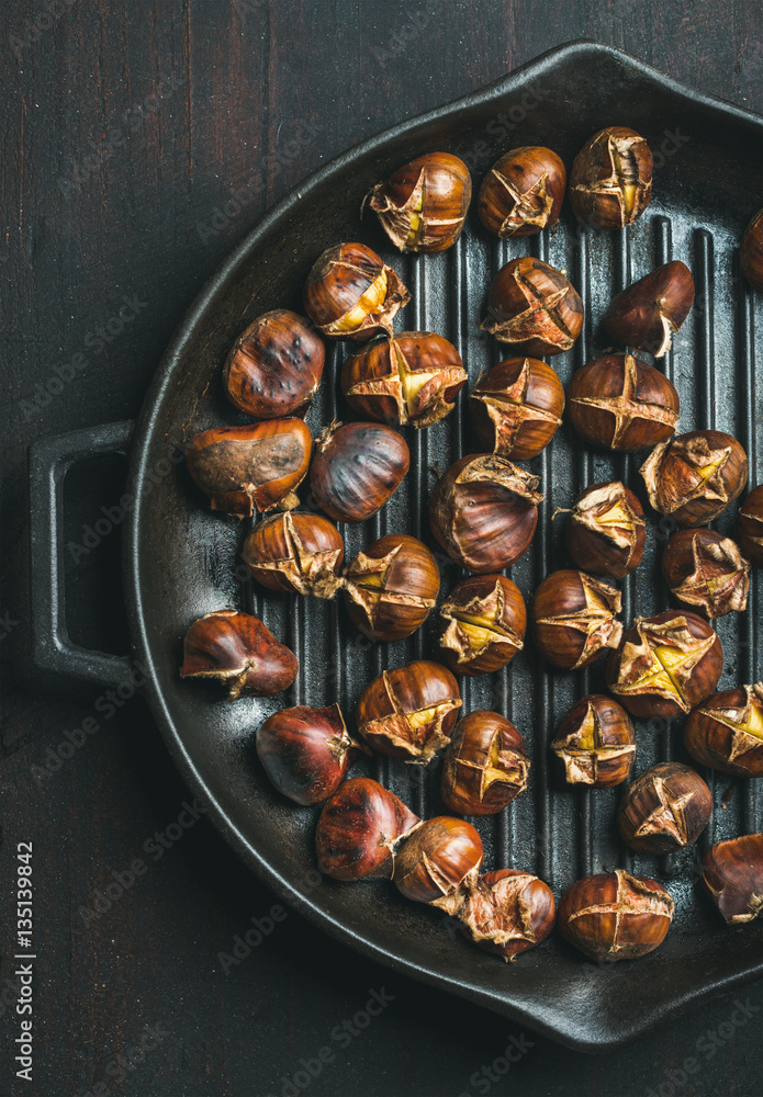 Roasted chestnuts in cast iron grilling pan over dark wooden background, top view, vertical composit