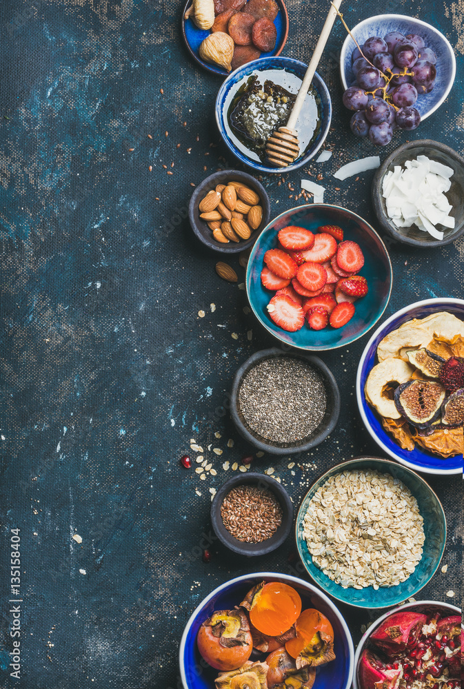 Ingredients for healthy breakfast in bowls over dark blue background, top view, copy space. Fresh an