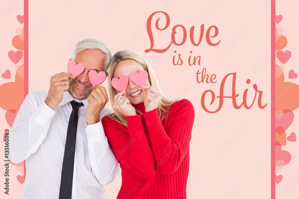 Composite image of silly couple holding hearts over their eyes