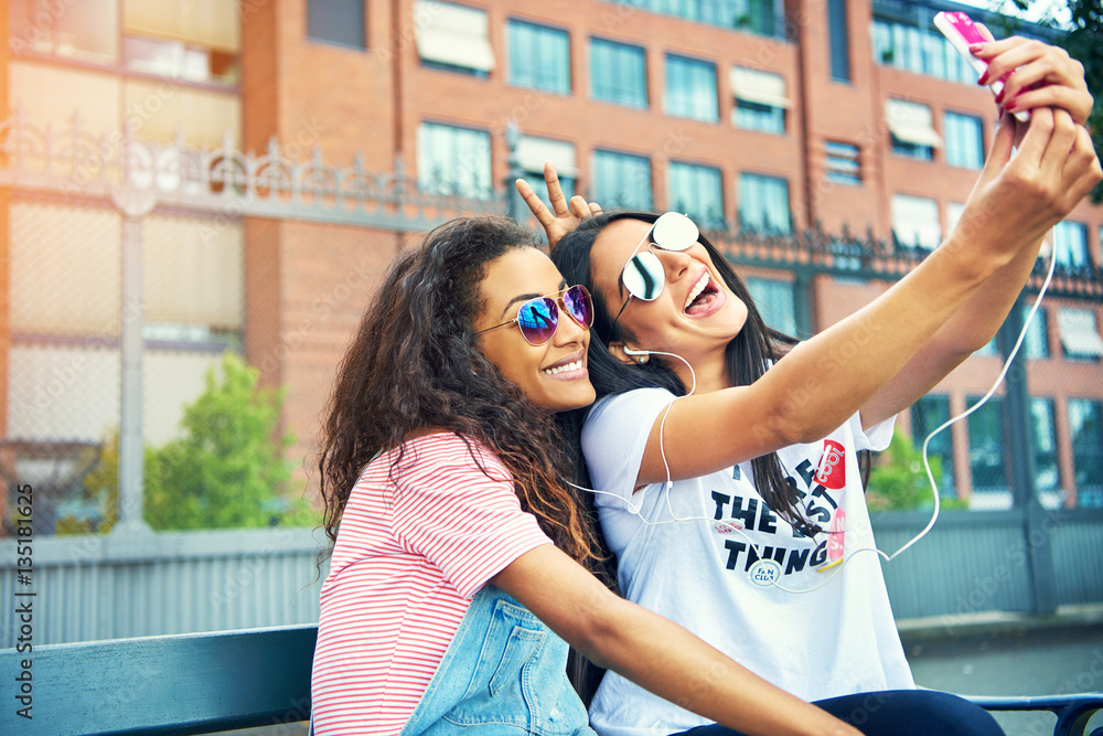 Giggling friends taking photos on bench