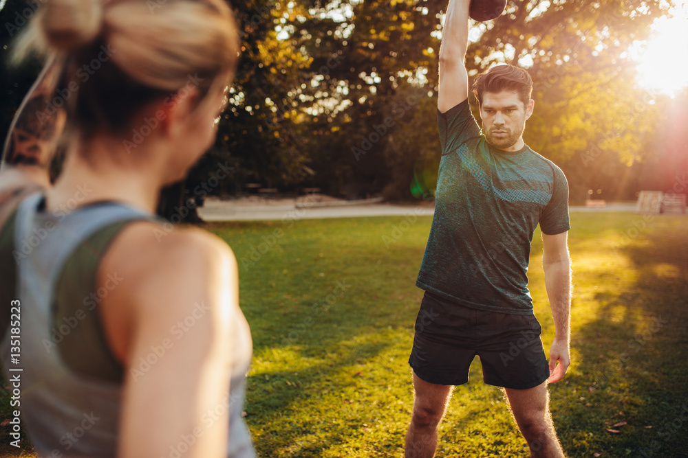 Healthy man exercising with personal trainer in park