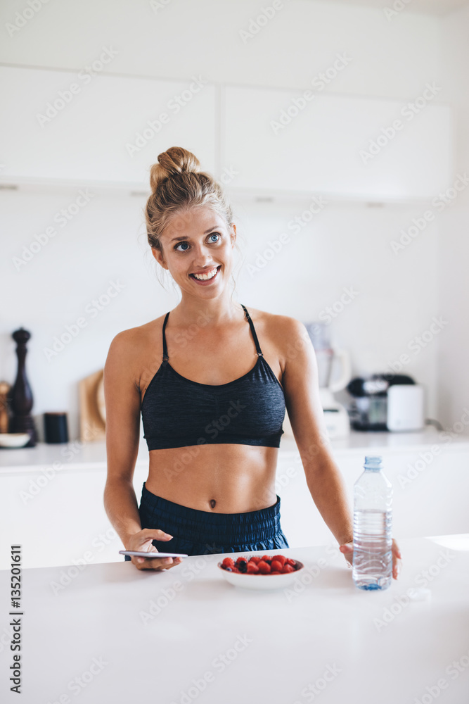 Young woman with berries in kitchen looking away smiling