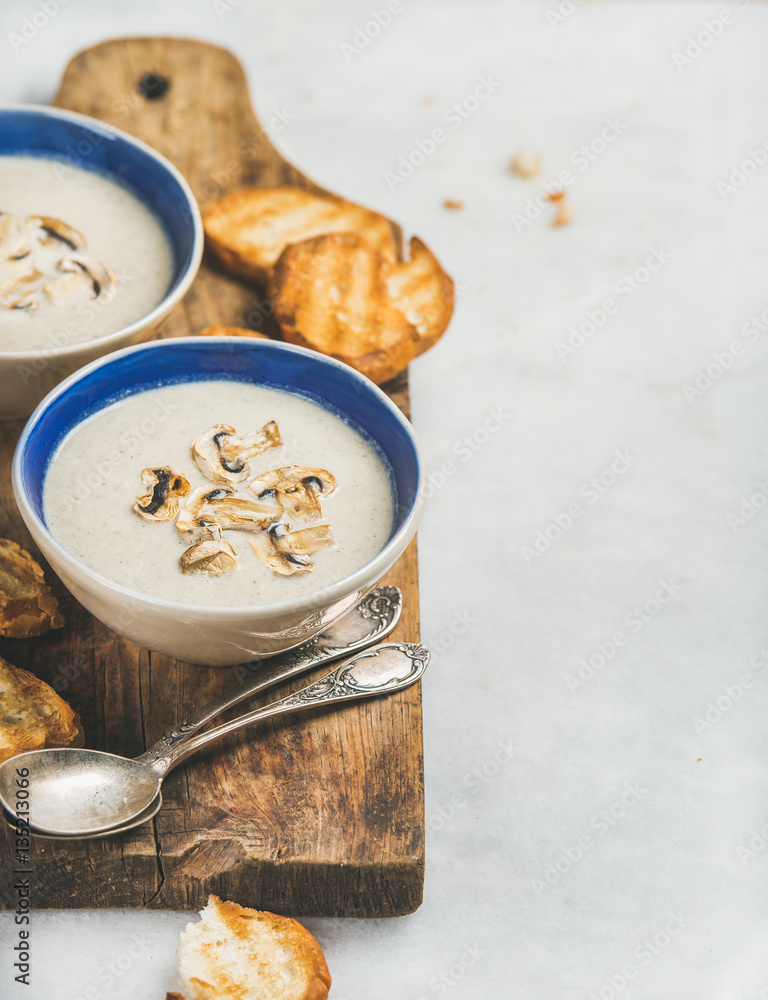 Healthy dinner with creamy mushroom soup in ceramic bowls and grilled bread slices on rustic serving