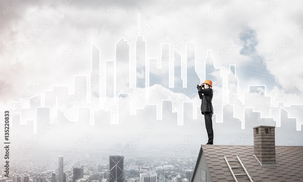 Engineer man standing on roof and looking in binoculars. Mixed m