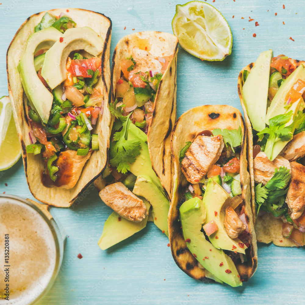 Healthy corn tortillas with grilled chicken, avocado, fresh salsa, limes and beer in glass over blue