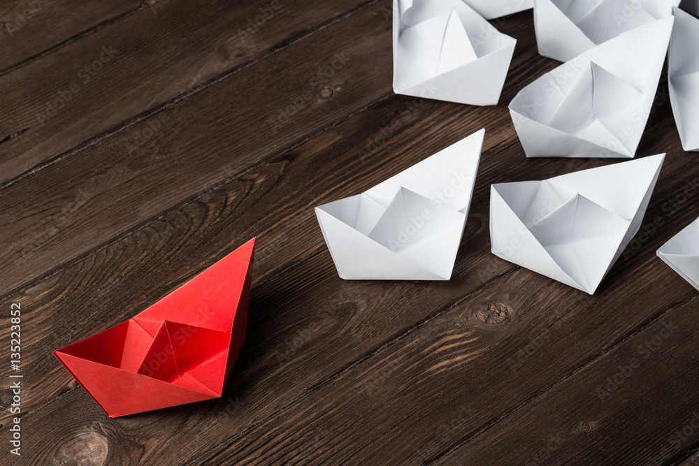 Business leadership concept with white and color paper boats on wooden table