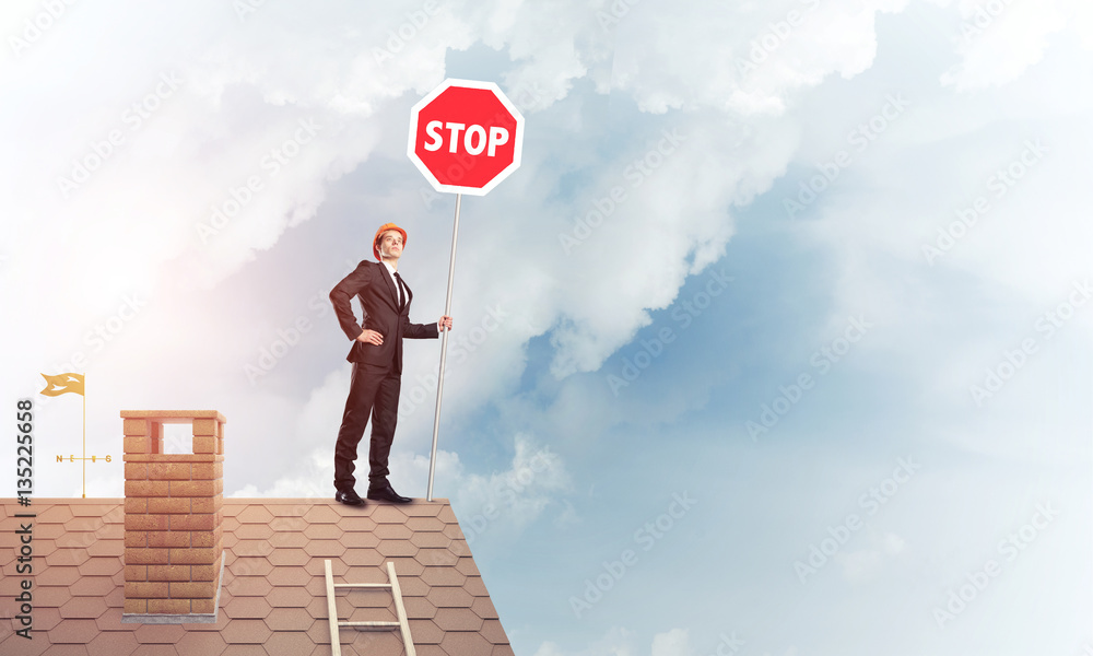 Caucasian businessman on brick house roof showing stop road sign