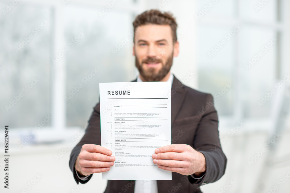 Elegant man in the suit holding resume for job hiring in the bright interior. Image focused on the f