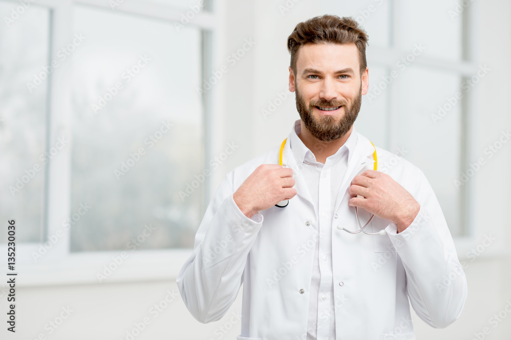 Portrait of a handsome doctor in uniform in front of the window in the white hospital interior