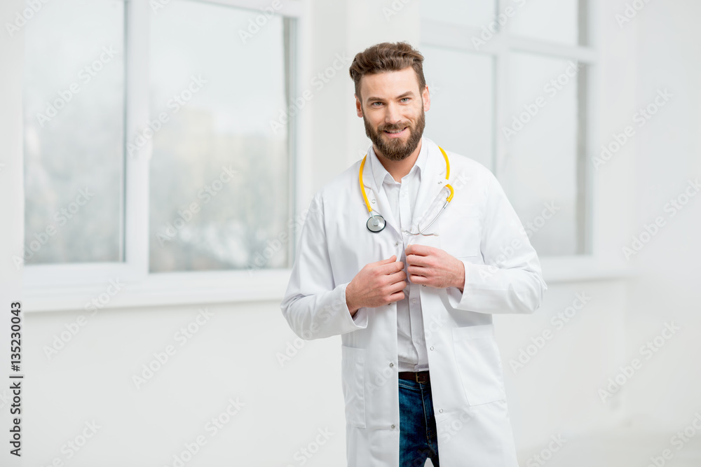 Portrait of a handsome doctor in uniform in front of the window in the white hospital interior