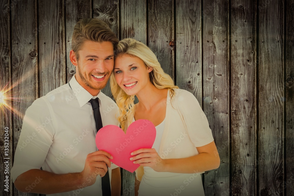 Composite image of attractive young couple holding pink heart