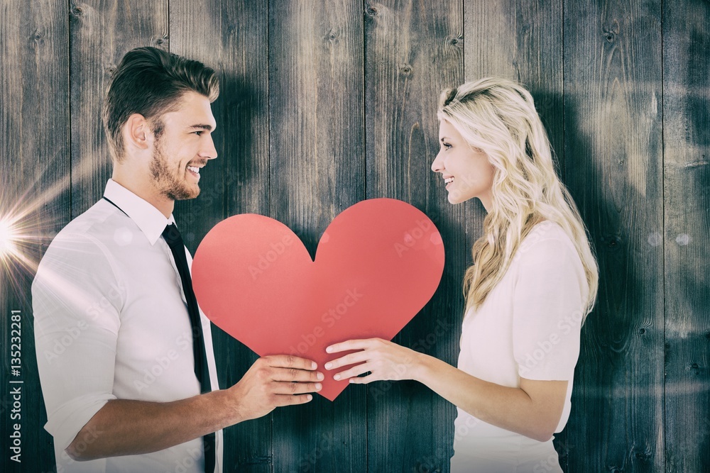 Composite image of attractive young couple holding red heart