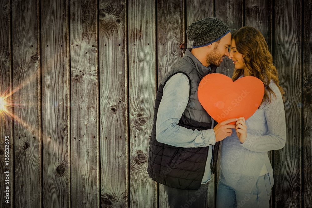 Composite image of happy young couple holding heart shape paper