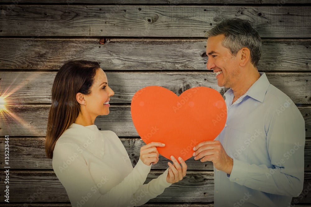 Composite image of smiling couple holding heart shape paper