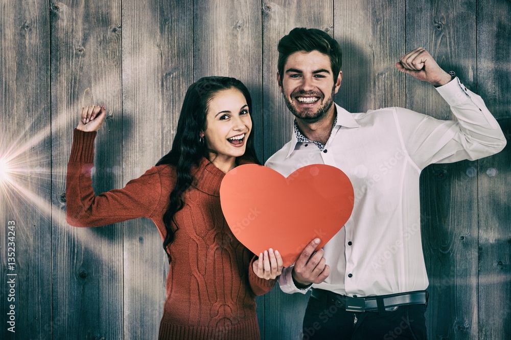 Composite image of cheerful couple holding paper heart