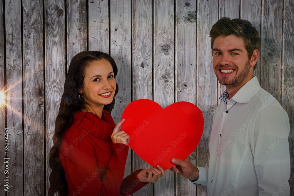 Composite image of smiling couple holding paper heart