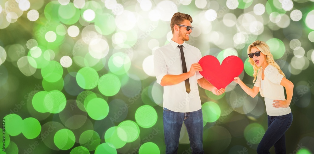 Composite image of cool young couple holding red heart