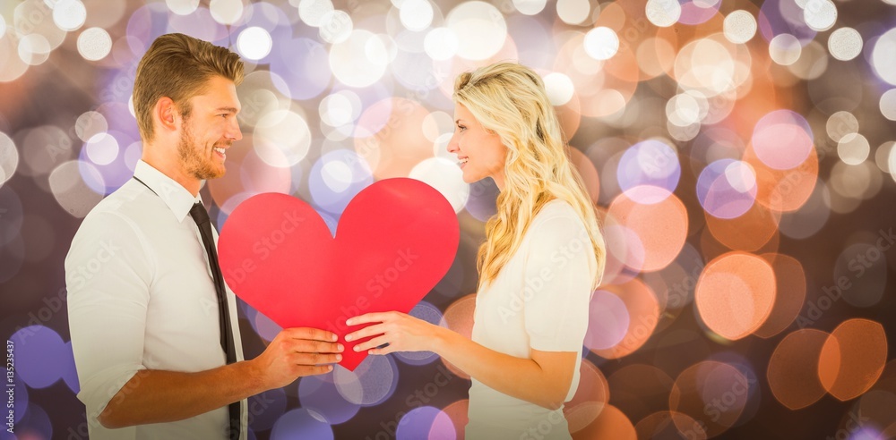 Composite image of attractive young couple holding red heart